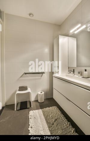 Ein modernes Bad mit weißen Wänden und schwarzen Fliesen auf dem Boden, es gibt einen großen Spiegel in der Ecke Stockfoto
