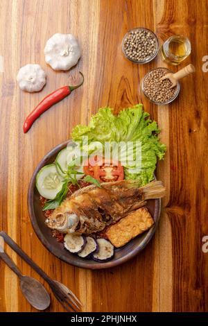 Knuspriger gebratener Fisch mit scharfer Chilisauce oder Sambal auf Töpferteller auf einem Holztisch Stockfoto