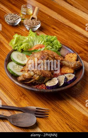 Knusprig gebratenes Hähnchen mit scharfer Chilisauce oder Sambal auf Töpferteller auf Holztisch Stockfoto