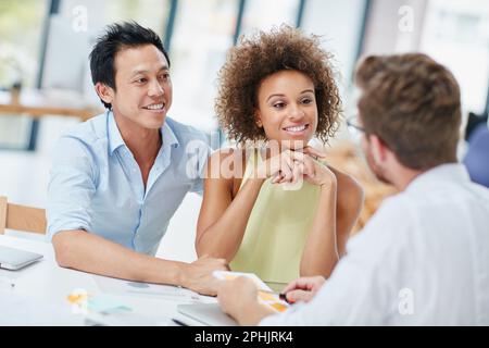Erzählen Sie uns mehr über Ihre Idee. Ein junges Paar trifft sich mit seinem Berater in seinem Büro. Stockfoto