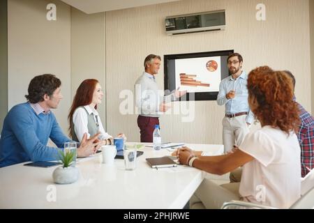 Die Zahlen werden veröffentlicht. Zwei Geschäftsleute, die ihren Kollegen bei der Arbeit eine Präsentation halten. Stockfoto