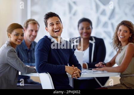 Zusammen waren wir ein tolles Team. Porträt einer Gruppe von lächelnden Kollegen, die zusammen an einem Tisch in einem Büro sitzen. Stockfoto