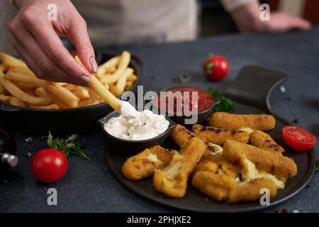 Frau taucht pommes in Dip-Sauce mit gebratenen Mozzarella-Stäbchen auf einem Tisch Stockfoto