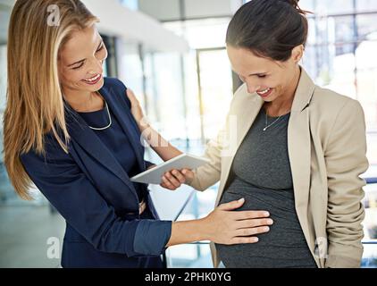 Du strahlst gerade. Eine Frau, die mit einem Kollegen über ihre Schwangerschaft spricht, während sie in einem modernen Büro steht. Stockfoto