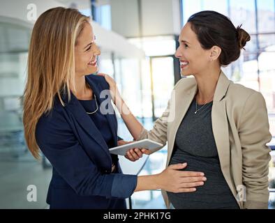 Mutterschaft steht dir so gut. Eine Frau, die mit einem Kollegen über ihre Schwangerschaft spricht, während sie in einem modernen Büro steht. Stockfoto
