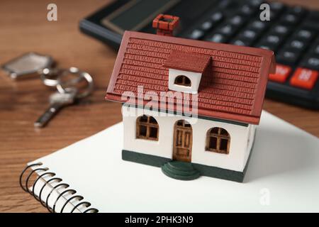 Hypothekenkonzept. Hausmodell, Notizbuch und Taschenrechner auf Holztisch, Nahaufnahme Stockfoto