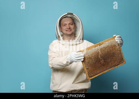 Imker in einheitlichem Bienenstockrahmen mit Wabenstruktur auf hellblauem Hintergrund Stockfoto