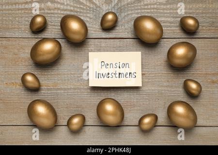 Goldene Eier und Karte mit Phrase Pensionsinvestitionen auf Holztisch, flach liegend Stockfoto