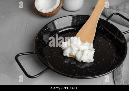 Bratpfanne mit Kokosöl und Holzspachtel auf hellgrauem Tisch Stockfoto