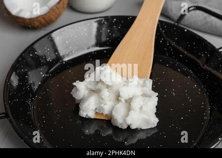 Bratpfanne mit Kokosöl und Holzspachtel auf hellgrauem Tisch, Nahaufnahme Stockfoto