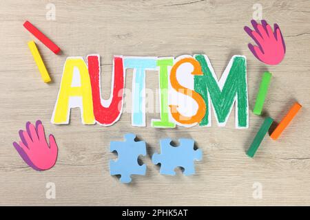 Wort Autismus aus Papier, Puzzleteilen und Buntstiften auf weißem Holztisch, flach liegend Stockfoto
