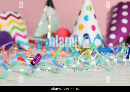 Farbenfrohe Schlangenbänder und anderes Partyzubehör auf weißem Holztisch, Nahaufnahme Stockfoto