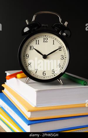 Wecker auf gestapeltem Buch neben der Tafel. Zeit für die Schule Stockfoto