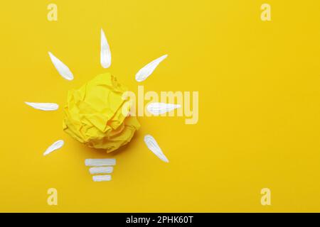 Komposition mit zerknitterter Papierkugel als Lampe auf gelbem Hintergrund, Draufsicht und Platz für Text. Ideenkonzept Stockfoto