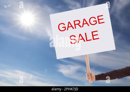 Ein Mann mit einem Schild mit TEXTNACHRICHT ZUM GARAGENVERKAUF vor blauem Himmel Stockfoto