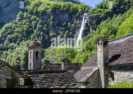 Die traditionellen Steinhäuser mit Kirchturm im wunderschönen Dorf Foroglio und der berühmte Wasserfall im Hintergrund, Tessin, Schweiz Stockfoto