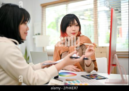 Zwei professionelle und talentierte asiatische Grafikdesignerinnen arbeiten gemeinsam an ihrem neuen Designprojekt im Studio. Teamarbeit und Zusammenarbeit Stockfoto