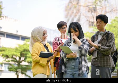 Eine Gruppe von netten jungen asiatischen Studenten ermutigen und trösten ihren traurigen Freund, während sie gemeinsam im Campuspark spazieren. Stockfoto