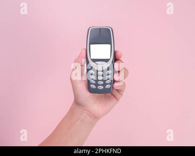 Nahaufnahme Hand hält Mobiltelefon Nokia 3310 isoliert auf pinkfarbenem Hintergrund. Weibliche Hand hält altes Telefon Nokia 3310. Stockfoto