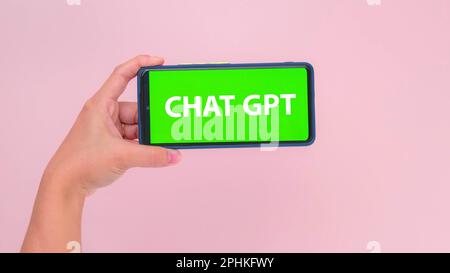 Mit der Hand gehaltenes Smartphone mit grünem Chat-GPT-Bildschirm in horizontaler Position isoliert auf pinkfarbenem Hintergrund. Chatbot-Assistent oder künstliches i Stockfoto