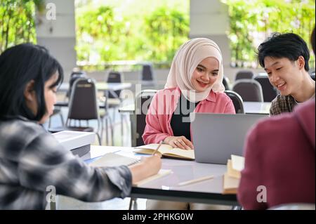 Eine wunderschöne, junge asiatische, muslimische Studentin macht ein Schulgruppenprojekt mit ihren Freunden in der Campuskantine. Stockfoto