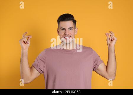 Hübscher Mann, der Finger auf gelbem Hintergrund schnappte Stockfoto