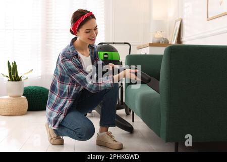 Junge Frau saugt Sofa im Wohnzimmer Stockfoto