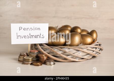 Goldene Eier im Nest, Münzen und Karte mit Phrase Pensionsinvestitionen auf weißem Holztisch Stockfoto
