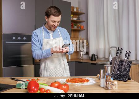 Ein gutaussehender Mann, der in der Küche kocht und mit seinem Handy fotografiert und Essen zubereitet Stockfoto