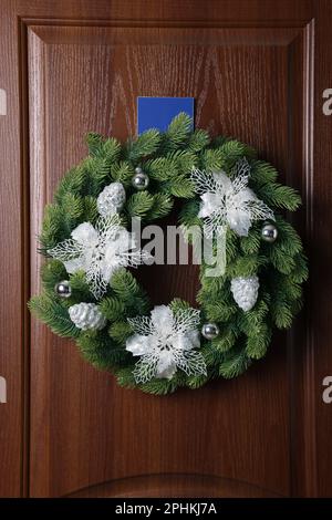 Wunderschöner Weihnachtskranz mit festlichem Dekor, das an einer Holztür hängt Stockfoto