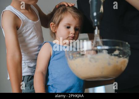 Eine Frau mit ihren beiden Kindern mixt Mehl, während sie Teig in der Schüssel zubereitet, und genießt es, hausgemachte Speisen zu kochen. Ich habe Spaß zu Hause. Backen mit Mutter. Stockfoto