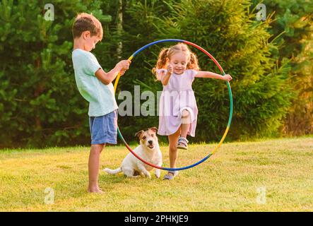 Kinder, die mit einem Hund spielen, der durch den Hula-Reifen springt Stockfoto