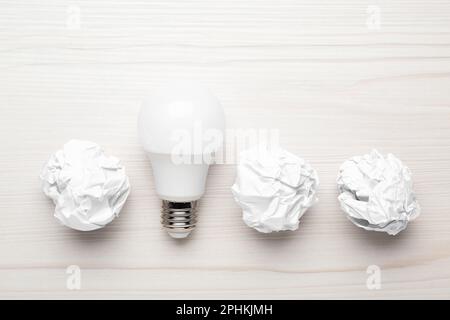 Kreative flache Laienzusammensetzung mit Glühbirne und Papierkugeln auf weißem Holztisch. Ideenkonzept Stockfoto
