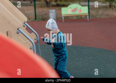 Ein kleiner Junge mit Down-Syndrom klettert die Treppe hoch, um zu rutschen Stockfoto