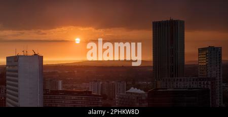 Ein rot-orangefarbener, warm leuchtender Sonnenuntergang vom Zentrum der Stadt. Blick über die Türme von Manchester bis zu den fernen Hügeln von hoch oben. Stockfoto