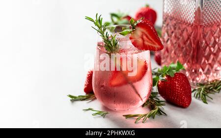 Erfrischendes Getränk mit natürlichem Eis, Erdbeeren und Rosmarin in einem gefrorenen Glas. Gin und Tonic Cocktail auf einem weißen Marmortisch. Speicherplatz kopieren. Stockfoto