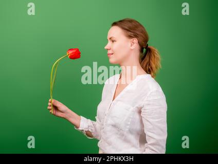 Eine hübsche Frau mittleren Alters, 40 Jahre alt, hat eine Blume - eine rote Tulpe auf grünem Hintergrund. Stockfoto