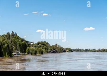 Upington, Südafrika - 24. Februar 2023: Ein Ausflugsboot und ein schwimmendes Restaurantdeck am Ufer eines überfluteten Orange River in Upington Stockfoto