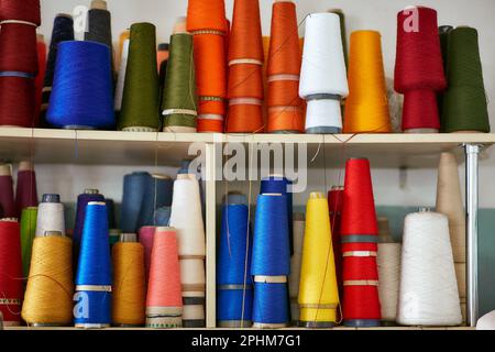 Viele Spulen mit Strickfäden stehen in einer Reihe auf einem Regal Stockfoto