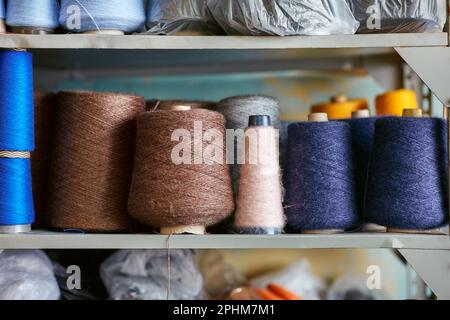 Spulen mit gestrickten Fäden stehen in einer Reihe auf dem Regal Stockfoto