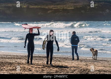 Ein männlicher und weiblicher Surfer, der am Fistral Beach spaziert, nachdem er eine Surftour in Newquay in Cornwall im Vereinigten Königreich beendet hat. Stockfoto