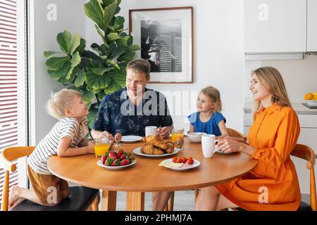 Glückliche Familie mit zwei Kindern, die am Tisch sitzen und morgens in der Küche frühstücken Stockfoto