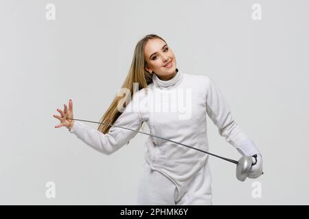 Teenager-Mädchen im Fechtkostüm mit Schwert in der Hand isoliert auf weißem Hintergrund. Fechtermädchen berührt die Spitze des Schwertes mit ihrer Hand. Stockfoto