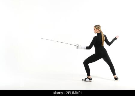 Teenager in einem schwarzen, eng anliegenden Overall, die mit einem Schwert auf weißem Hintergrund trainiert Stockfoto