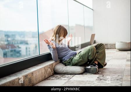 Ein wunderschöner Teenager-Influencer in sozialen Medien, der auf dem Terrassenboden sitzt und ein Notebook zum Lernen und zur Unterhaltung benutzt Stockfoto