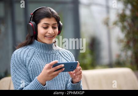 Junge Frau Im Freien Mit Kabellosen Kopfhörern, Die Sich Einen Film Oder Streaming-Film Auf Dem Mobiltelefon Ansieht Stockfoto