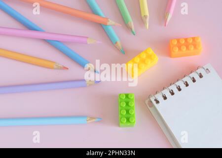 Pastellfarbene Bleistifte mit Notizblock, Draufsicht auf pinkfarbenem Hintergrund, Back-to-School-Konzept Stockfoto