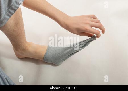 Boy zieht graue Socken an, man legt Socken in kaltem Winter an oder zieht es zu Hause aus Stockfoto