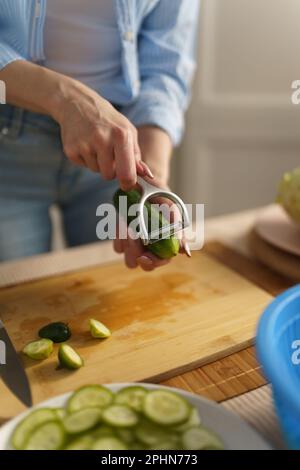 Hausfrau schält Gurke mit einem Schälwerkzeug in Nahaufnahme ab. Eine Frau schält zu Hause Gemüse zum Mittagessen Stockfoto