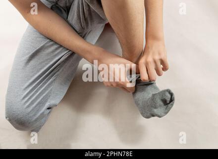 Boy zieht graue Socken an, man legt Socken in kaltem Winter an oder zieht es zu Hause aus Stockfoto